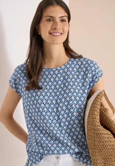 Vrouw met blauw-wit dessin T-shirt, draagt een gevlochten mand onder haar arm.