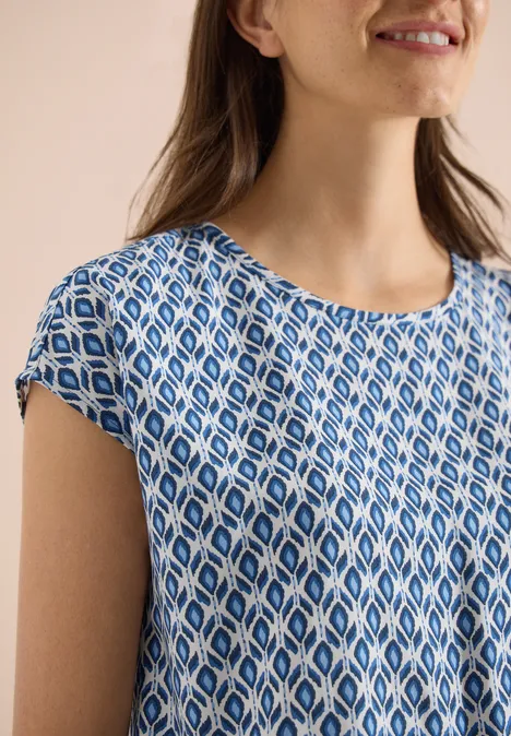 Close-up van een vrouw met een blauw-wit dessin top met korte mouwen.
