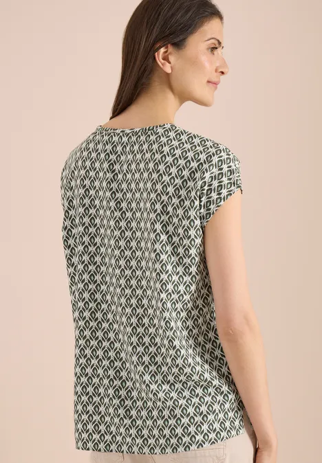Vue de dos d'une femme portant un top vert à manches courtes orné d'un motif géométrique blanc.