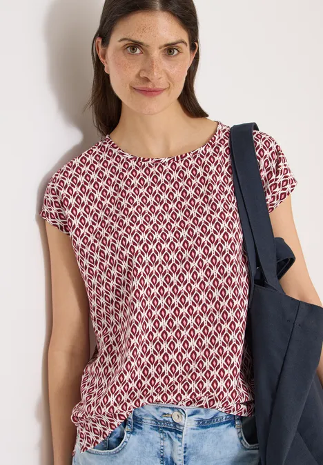 Une femme porte un haut à manches courtes rouge et blanc et un sac épaule bleu foncé.