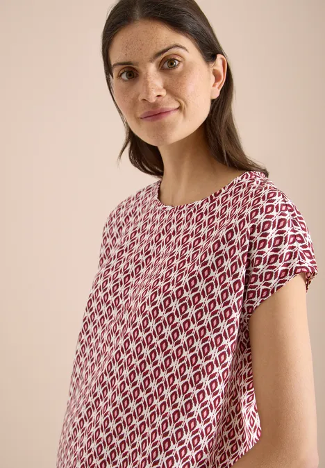 Femme porte un t-shirt ample à motif losanges rouge et blanc sur fond clair