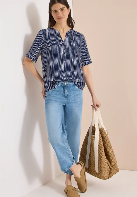 Vrouw met blauw dessinblouse, lichte jeans, platte schoenen en grote shopper.