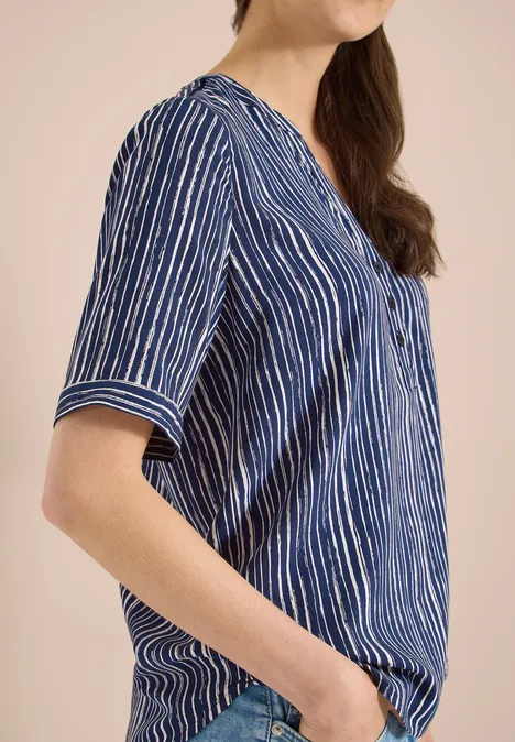 Een vrouw draagt een blauw-wit gestreepte blouse met korte mouwen en V-hals.