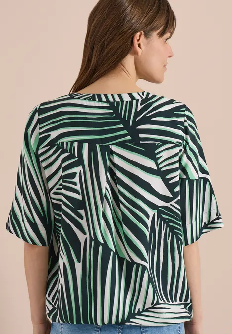 Achteraanzicht van een model in een losse blouse met tropische, groen-witte bladprint.