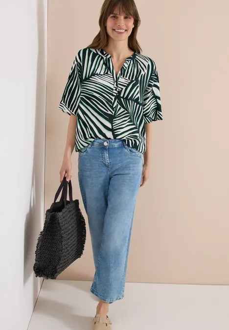 Dame draagt kortedarm overhemd met groen-wit zebrapatroon, blauwe rechte cropped jeans en zwarte gevlochten shopper.