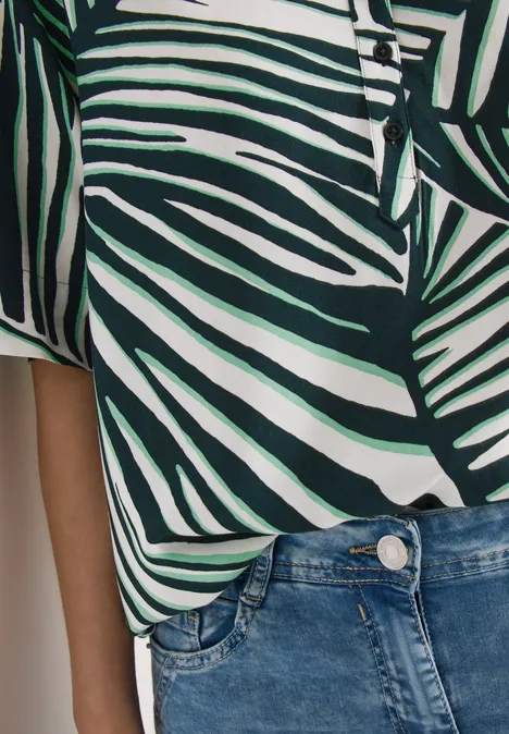 Wit-groen shirt met palmbladerenprint en blauwe spijkerbroek.