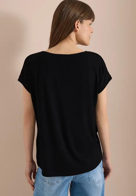 Blouse avec col rond et détail de nœuds Black Vue de dos d'une personne portant un t-shirt noir ample et un jean bleu clair sur fond neutre.