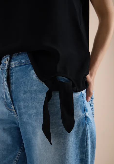 Blouse avec col rond et détail de nœuds Black Jean bleu clair et top noir avec un nœud sur le côté à la taille.