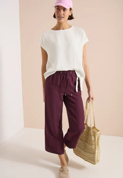Femme en haut blanc, pantalon large bordeaux et sac en paille.