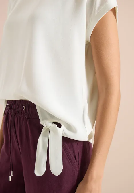 Chemisier blanc ample et pantalon bordeaux à taille élastiquée avec nœud décoratif.