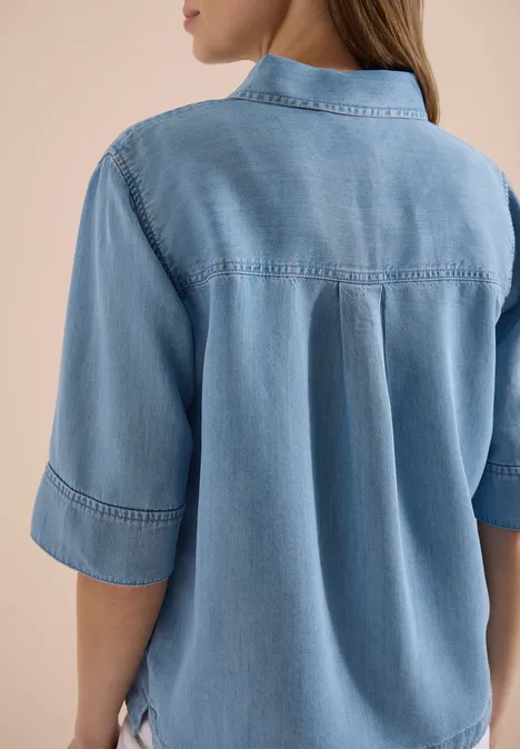 Achteraanzicht van iemand in een lichtblauw denimblouse met opgerolde mouwen.