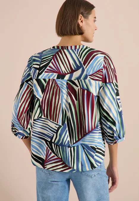 Frau von hinten in gemusterter Bluse mit geometrischen Streifen in Blau, Grün, Rot und Weiß.
