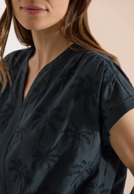 Vrouw draagt een donkere top met korte mouwen en subtiel patroon, V-hals.