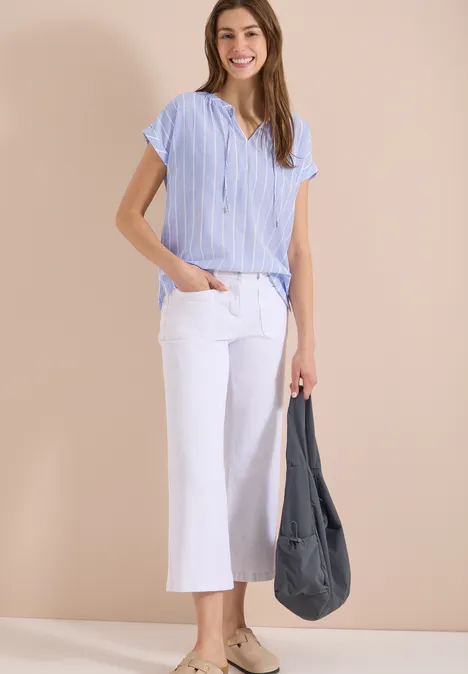 Modell in hellblau-weiß gestreifter Bluse, weißen Culottes und grauer Tasche vor beigem Hintergrund.