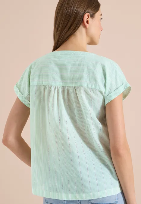 Frau von hinten in hellgrün-gestreifter Kurzarmbluse, steht entspannt.