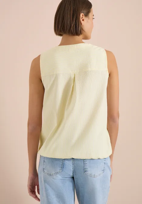 Femme vue de dos portant un débardeur jaune pâle et un jean bleu.