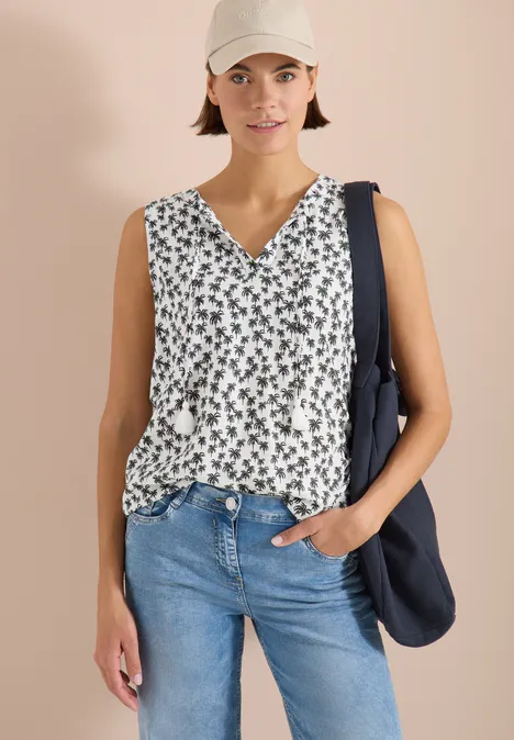 Vrouw met witte mouwloze bloes met bloemenpatroon, blauwe jeans en donkerblauwe schoudertas.