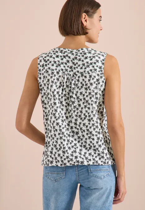 Vrouw van achteren in een blauwe jeans en mouwloze witte top met zwart bloemenpatroon.