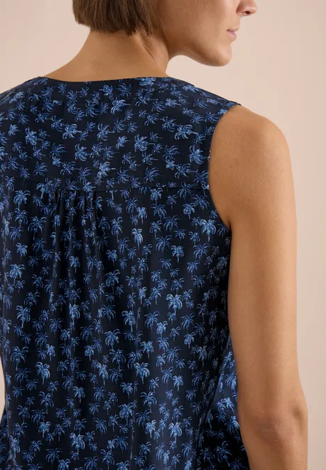 Vrouw gezien van achteren in een mouwloos donkerblauw topje met blauw bloemenpatroon en rugplooien.