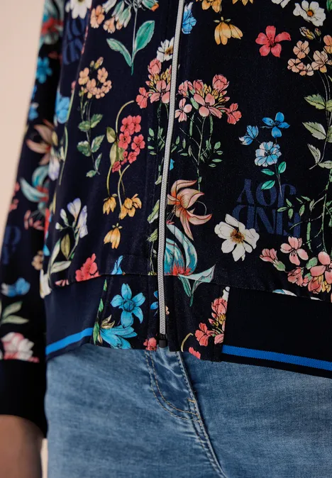 Nahaufnahme eines dunklen, bunt geblümten Oberteils mit Reißverschluss und hellblauen Jeans.