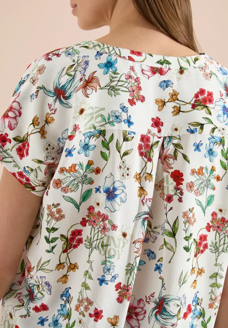 Close-up van een witte blouse met kleurrijke bloemprint en losjes geplooide rugpartij.