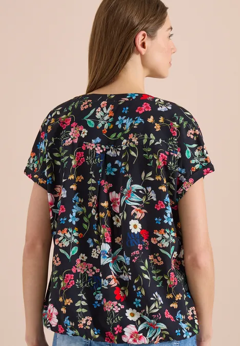 Achteraanzicht van een vrouw in een zwarte, kort mouwbloes met kleurrijke bloemenprint.