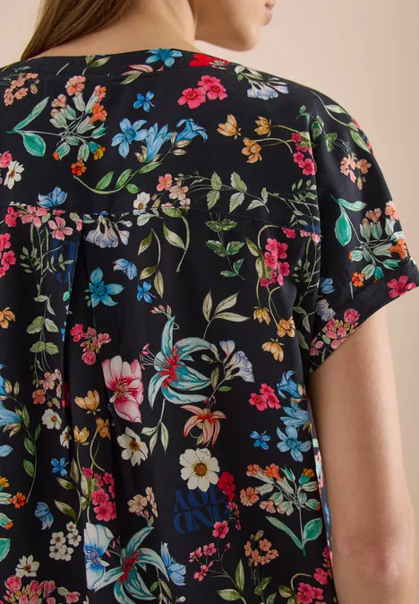 Achteraanzicht van een vrouw in een zwart T-shirt met korte mouwen en kleurrijke bloemenprint.