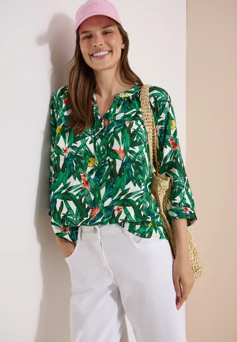 3/4-Arm Tunika mit Split Neck und Print khaki Frau in grüner, tropischer Bluse, weißen Hosen, rosafarbenem Hut und Korbtasche.