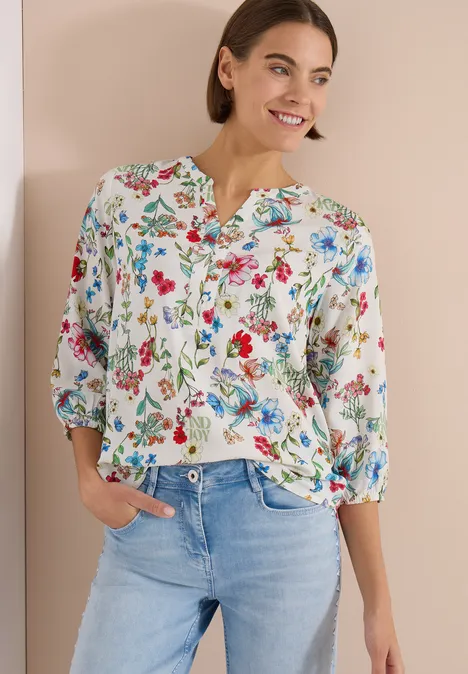 Frau trägt weiße Bluse mit buntem Blumenmuster und hellblaue Jeans