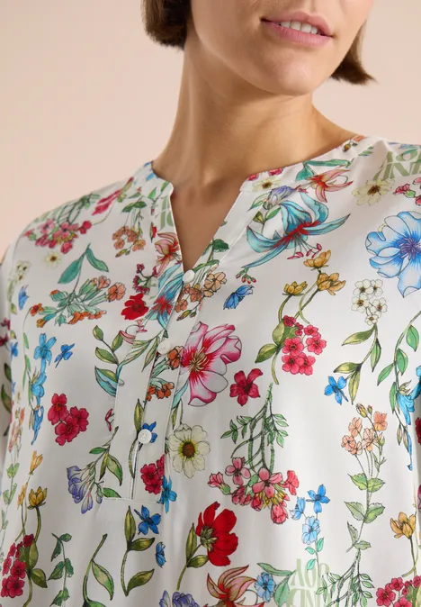 Frau trägt weiße Bluse mit buntem Blumenmuster und V-Ausschnitt.