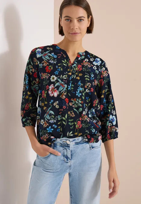 3/4-Arm Bluse mit Split Neck und Print universal blue Frau trägt schwarze Bluse mit buntem Blumenmuster und halblangen Ärmeln zu hellblauen Jeans.