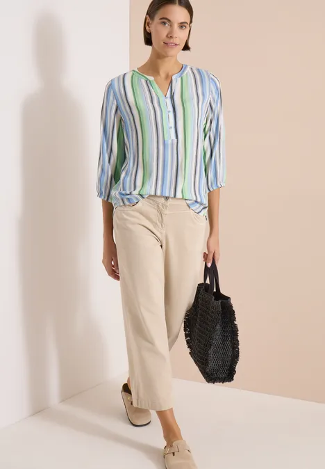 Frau in gestreifter Bluse, heller Culotte-Hose, weißen Plateauschuhen und schwarzer Flecht-Tasche.