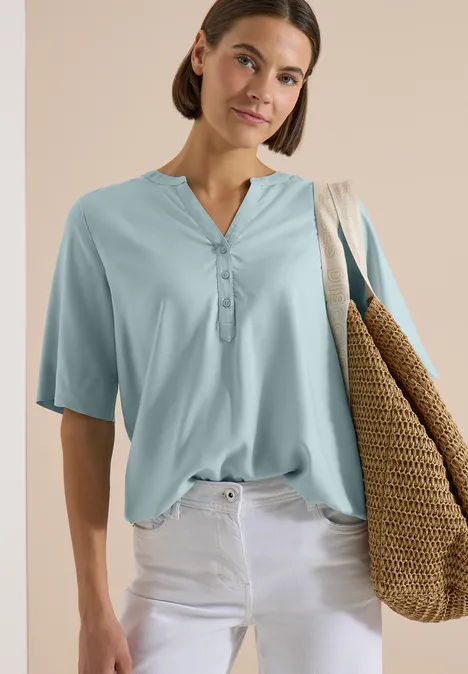 Blouse met korte mouwen en gespleten hals crystal mint Frau in hellblauer Bluse mit kurzem Arm, weißer Hose und großer geflochtener Tasche.