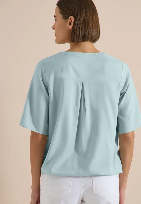 Blouse met korte mouwen en gespleten hals crystal mint Rückenansicht einer Frau mit kinnlangen Haaren, hellblauer Bluse mit Rückenfalte und weißen Hosen.