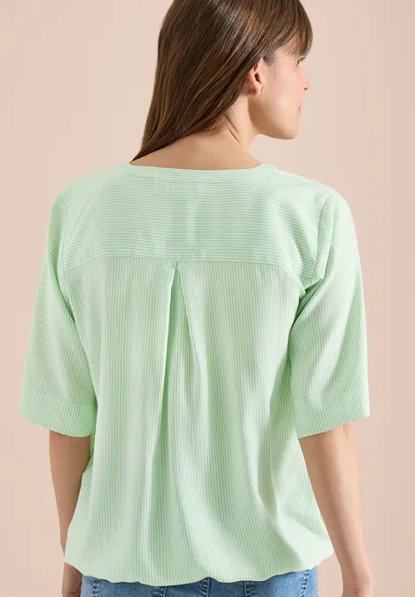 Frau von hinten in lockerem, pastellgrünem Oberteil mit halblangen Ärmeln und Rückenfalte.