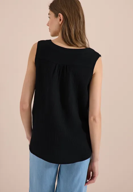 Frau von hinten in schwarzem ärmellosem Top und blauen Jeans vor neutralem Hintergrund.