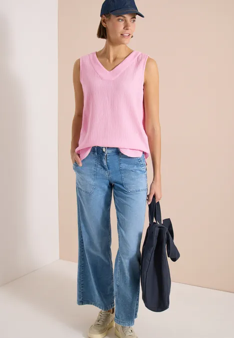 Frau in pinkem V-Ausschnitt-Top und weiten Jeans hält navyblauen Beutel.