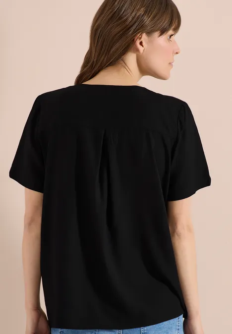 Rugaanzicht van een vrouw in een zwart shirt met korte mouwen voor een neutrale achtergrond.