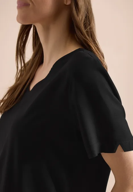 Een vrouw in profiel draagt een eenvoudig zwart T-shirt met V-hals en korte mouwen.