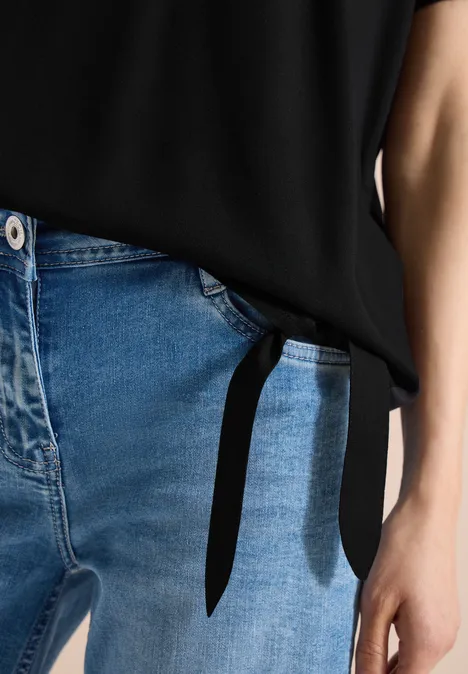 Close-up van een taille in blauwe jeans en een zwart geknoopt topje.