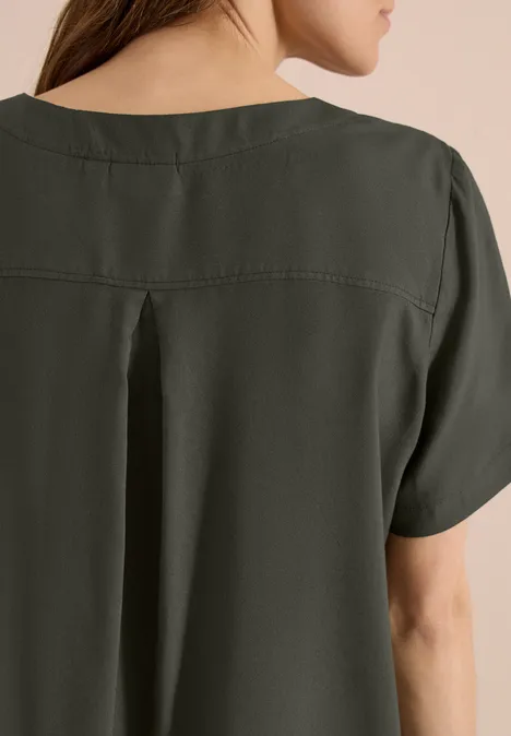 Rückenansicht einer Frau in olivgrünem, kurzärmligem Oberteil mit Kellerfalte und weitem Schnitt