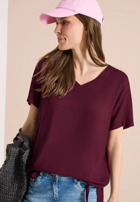 Vrouw draagt een bordeauxroze V-hals T-shirt met korte mouwen en een spijkerbroek.