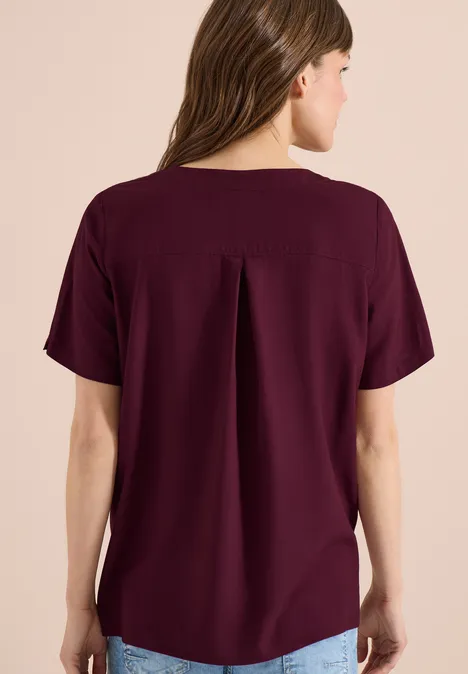 Achteraanzicht van een vrouw in losvallende, bordeauxrode top met korte mouwen