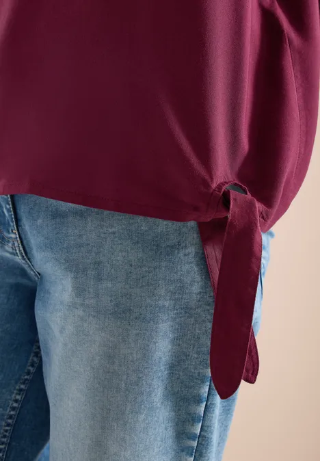 Close-up van een spijkerbroek en een bordeauxrode top met een knoop aan de zijkant.