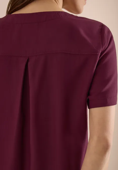 Vrouw van achteren in een bordeauxkleurige top met korte mouwen.