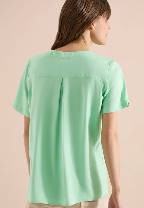 Vrouw van achteren in losvallende mintgroene blouse met korte mouwen.