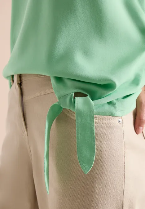 Close-up van een groen bovenstuk met zijstrik en beige broek.