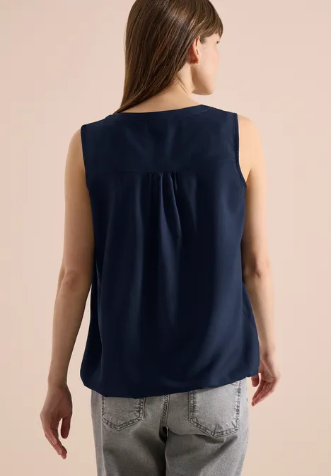 Rückenansicht einer Frau in navy ärmelloser Bluse und grauer Jeans.