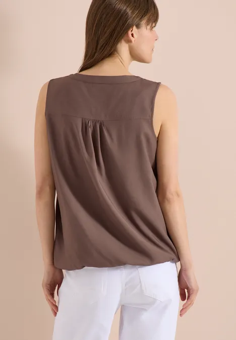 Frau von hinten in ärmellosem braunen Top und weißen Hosen