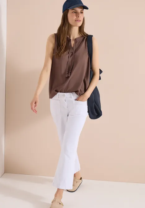 Frau in braunem Top, weißer Caprihose, blauer Schirmmütze und Schultertasche